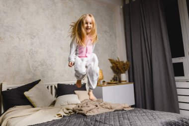Pijamalı mutlu kız çocuğu atlıyor ve yatakta oynuyor.