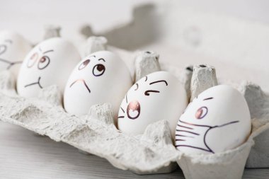 Karalama yüzlü tavuk yumurtaları kutuda tıbbi maskeler takıyor. Beyaz yumurta kabuğundaki beyaz kalem duygularıyla çizilmiş epidemi 2020 Coronavirüs için maskeli ve izole edilmiş Paskalya tatili için evde..