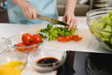 Gemide kesilmiş yeşil salata var. Kadın elleri taze yeşil salata hazırlar ve mutfak arka planındaki şeffaf kaseye malzemeler koyar..