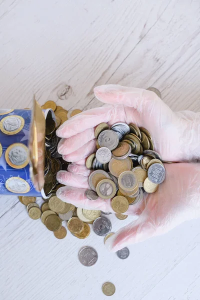 Hands in plastic polyethylene transparent gloves hold coins different currency from piggy bank during epidemy, financial and economic crisis