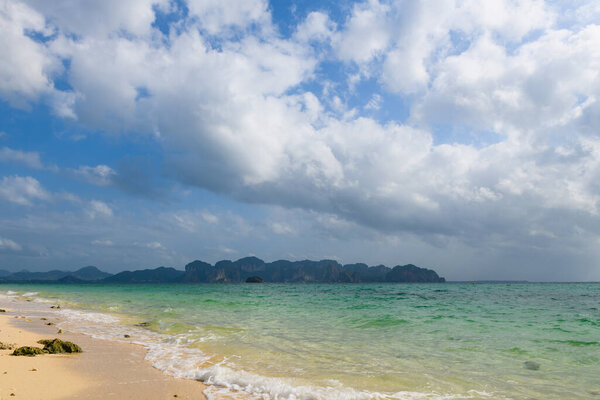 Scenic marine background of Krabi Poda Chicken island beach with white sand, cloudy sky and sea waves at windy day