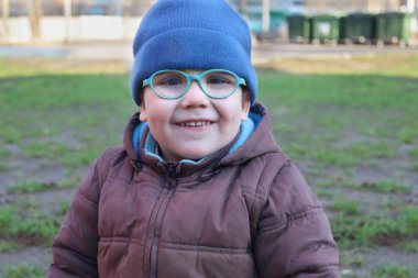 Gözlük ve sıcak giysiler mutlu küçük çocuk kameraya benziyor 