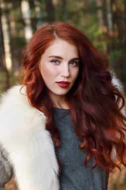 Güzel kız beyaz kürklü orman güneşli, kamerada bakar 