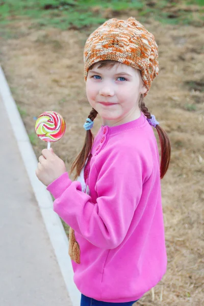 Happy little girl in pink walks with bright lollipop outdoor — Stock Photo, Image