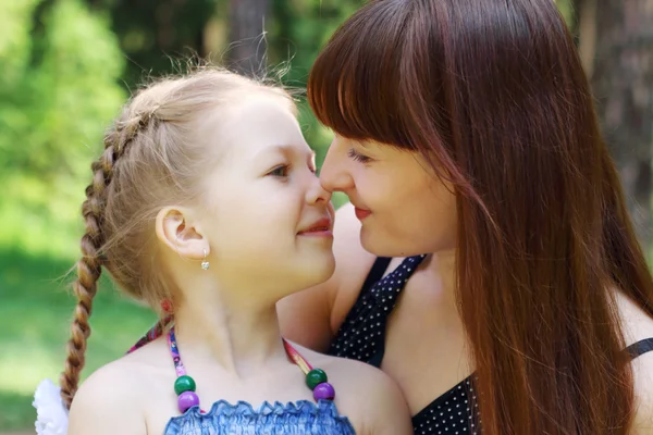 Happy mother and daughter rub noses in park at summer sunny day — Stock Photo, Image