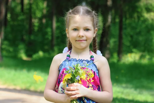 Happy little cute girl poses with flowers in sunny park — Stock Photo, Image