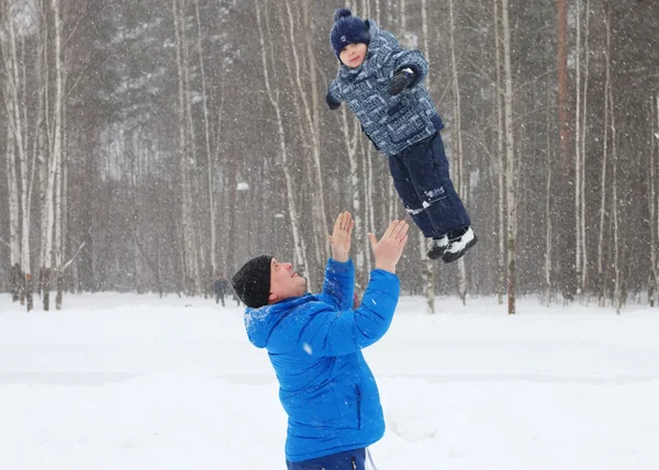 Lycklig far kastar upp hennes unge son i parken under snöfall — Stockfoto