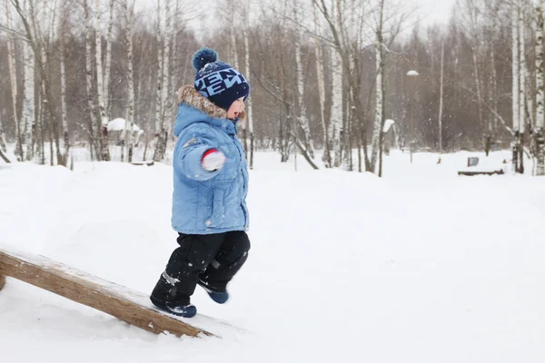 Glad liten pojke körs på logg i parken under snöfall på vintern — Stockfoto