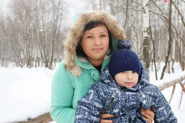 Lycklig mamma med sin lilla son under snöfall i vinterdag — Stockfoto