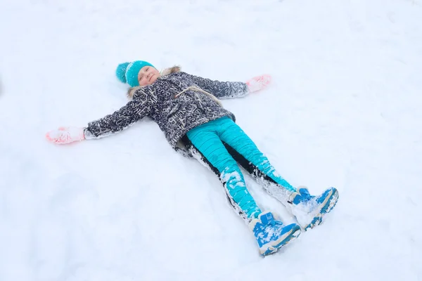 Glad tjej ligger på snö och spelar Angel under snöfall — Stockfoto