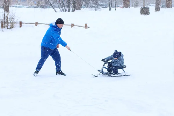 Счастливый отец играет с маленьким сыном на сноуборде во время снегопада — стоковое фото