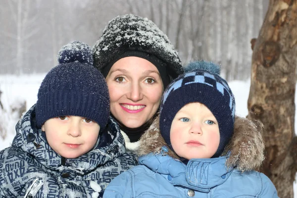 Mãe feliz com dois filhos sorrir no dia de inverno durante a queda de neve — Fotografia de Stock
