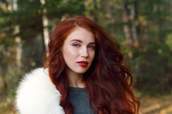 Hübsche Frau mit rot gelockten Haaren und Fell posiert im Wald — Stockfoto