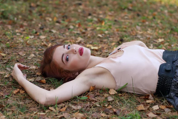 Красивая девушка в юбке с поясом лежит на сухой листве осенью — стоковое фото