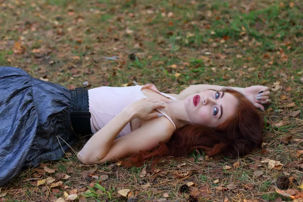 Piękna kobieta w spódnicy z pasem leży na suchych liści jesienią — Zdjęcie stockowe