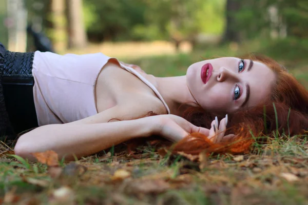 Beautiful girl lies on dry leaves and looks at camera in autumn — Stock Photo, Image