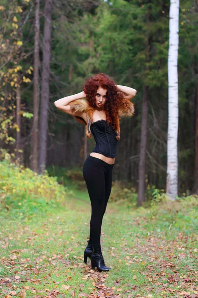 Pretty young woman in corset with fur stands in autumn forest — Stock Photo, Image