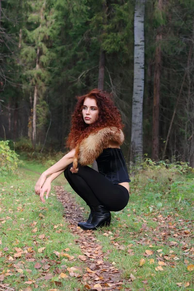 Pretty young woman in corset with fur squatting in autumn forest — Stock Photo, Image