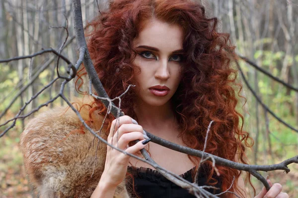 Beautiful girl with curly hair poses among tree branches — Stock Photo, Image