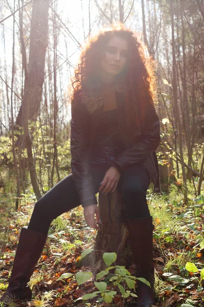 Schönes Mädchen in Stiefeln und Jacke auf Baumstumpf sitzend — Stockfoto