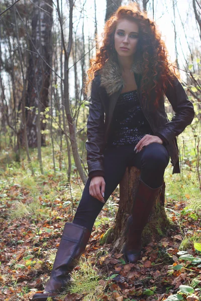 Beautiful girl in boots and jacket poses on tree stump — Stock Photo, Image