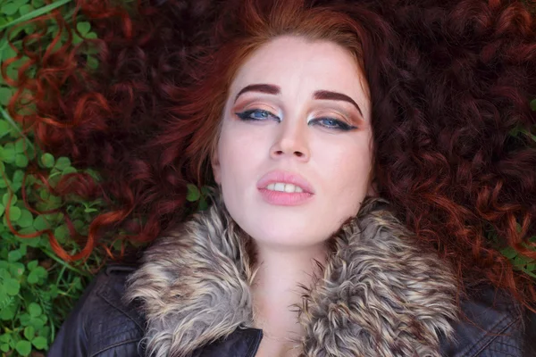 Hübsches Mädchen mit rotgelockten Haaren liegt auf grünem Kleefeld — Stockfoto
