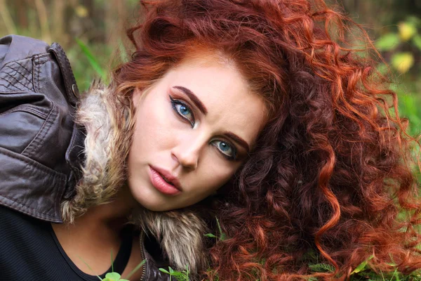 Pretty woman with curly hair in jacket on grass in field — Stock Photo, Image