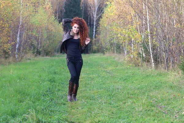 Pretty young woman in leather jacket stands on grass in autumn — Stock Photo, Image