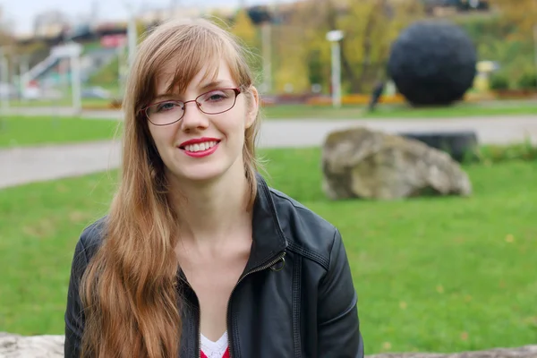 Mulher bonita em óculos em jaqueta de couro sorri no parque — Fotografia de Stock