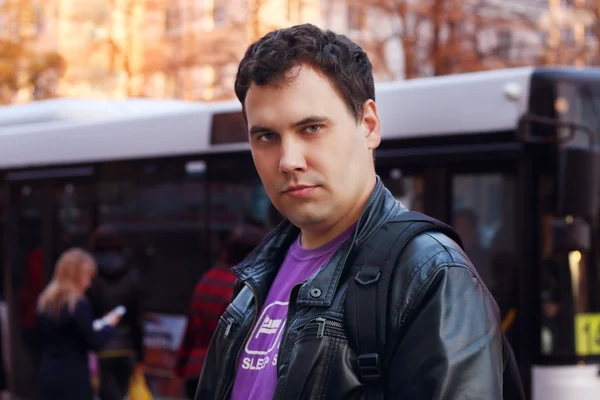 Man in leather jacket stands on street near bus stop in city — Stock Photo, Image