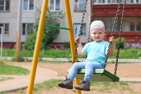 Little cute girl in hat swings on children playground at summer — Stock Photo, Image