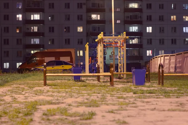Детская игровая площадка ночью возле здания и машины ночью — стоковое фото