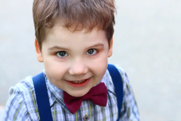 Happy little boy with bow tie smiles and looks at camera — Stock Photo, Image