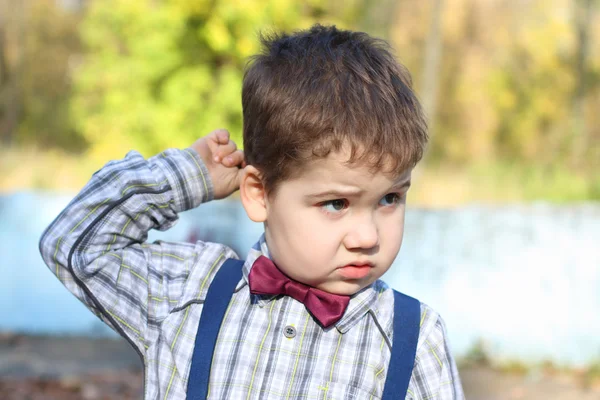 Regordete niño en camisa y pajarita piensa y rasca su h —  Fotos de Stock