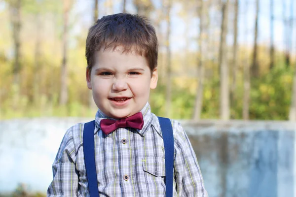 Bonito menino gordo na camisa e gravata borboleta grimaces em ensolarado — Fotografia de Stock
