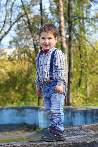 Plump little boy with bow tie and jeans stands in grimaces in su — Stock Photo, Image