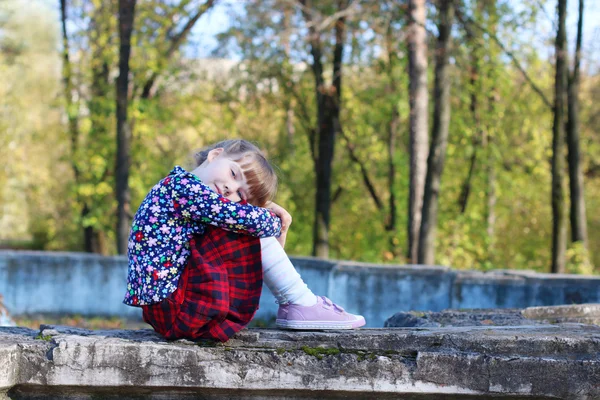 Cute little girl in red skirt sits on old fountain in sunny gree — Stock Photo, Image