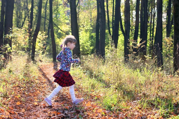 Cute little girl in red skirt runs in sunny green park with dry — Stock Photo, Image