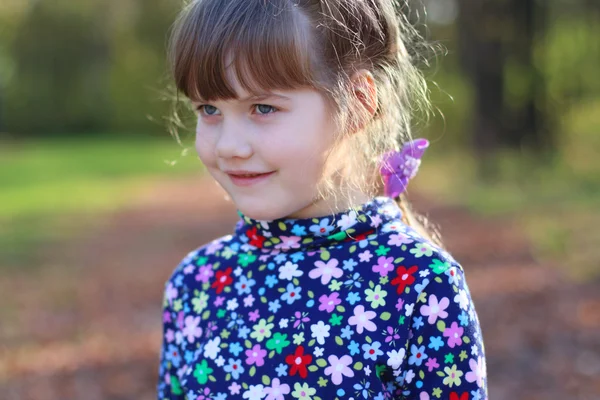 Happy little girl smiles in sunny green park, shallow dof, close — Stock Photo, Image