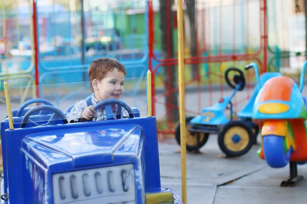 Zadowolony ładny mały chłopiec jeździ na samochód karuzela w letni dzień w — Zdjęcie stockowe