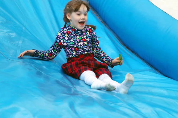 Happy little cute girl rides on inflatable slide outdoor in park — Stock Photo, Image