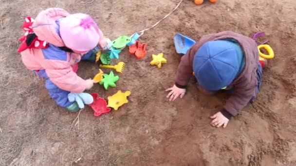 Счастливая девочка и мальчик играют с пластиковыми игрушками в песке — стоковое видео