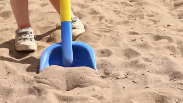 Spielzeugschaufel und Füße eines kleinen Jungen gehen im Sommer auf Sand — Stockvideo