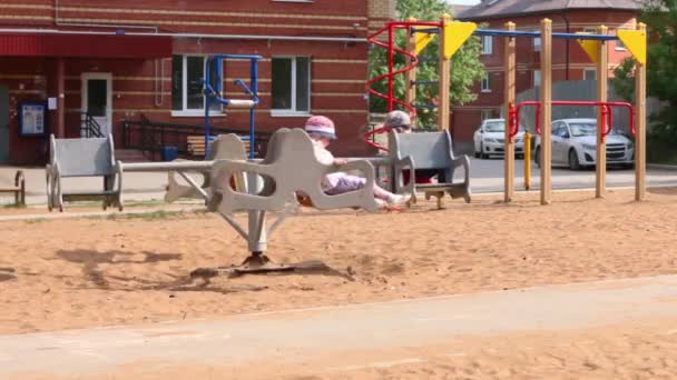 Jongen en meisje rit rotonde op speelplaats op zomerdag — Stockvideo