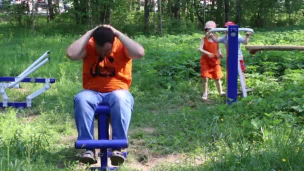 Vader en twee kleine meisjes doen oefeningen op outdoor sporters in groen park — Stockvideo