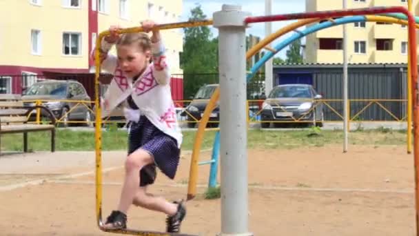 Маленькая девочка в платье играет на детской площадке в летний день — стоковое видео