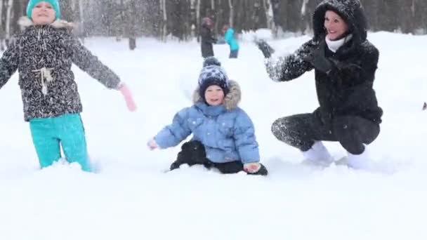 Mother, girl and little boy throw up snow during snowfall in winter park — Stock Video