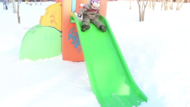 Feliz niño se desliza hacia abajo en invierno día soleado en el patio de recreo — Vídeos de Stock