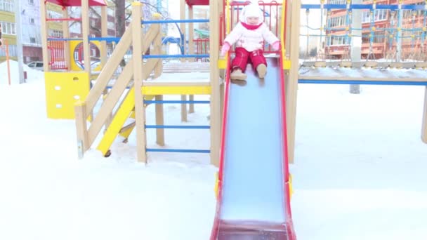 Happy little girl slides down on playground at winter sunny day — Stock video