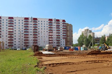 İşçiler, traktör, kum ve çim üzerinde eksilerini bina yakınındaki alanıyla